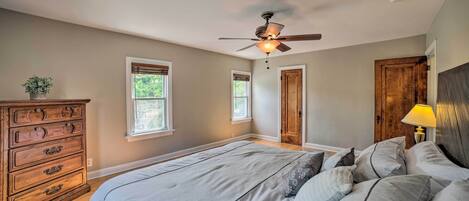 A bedroom with a bed, dresser, ceiling fan, and two windows.