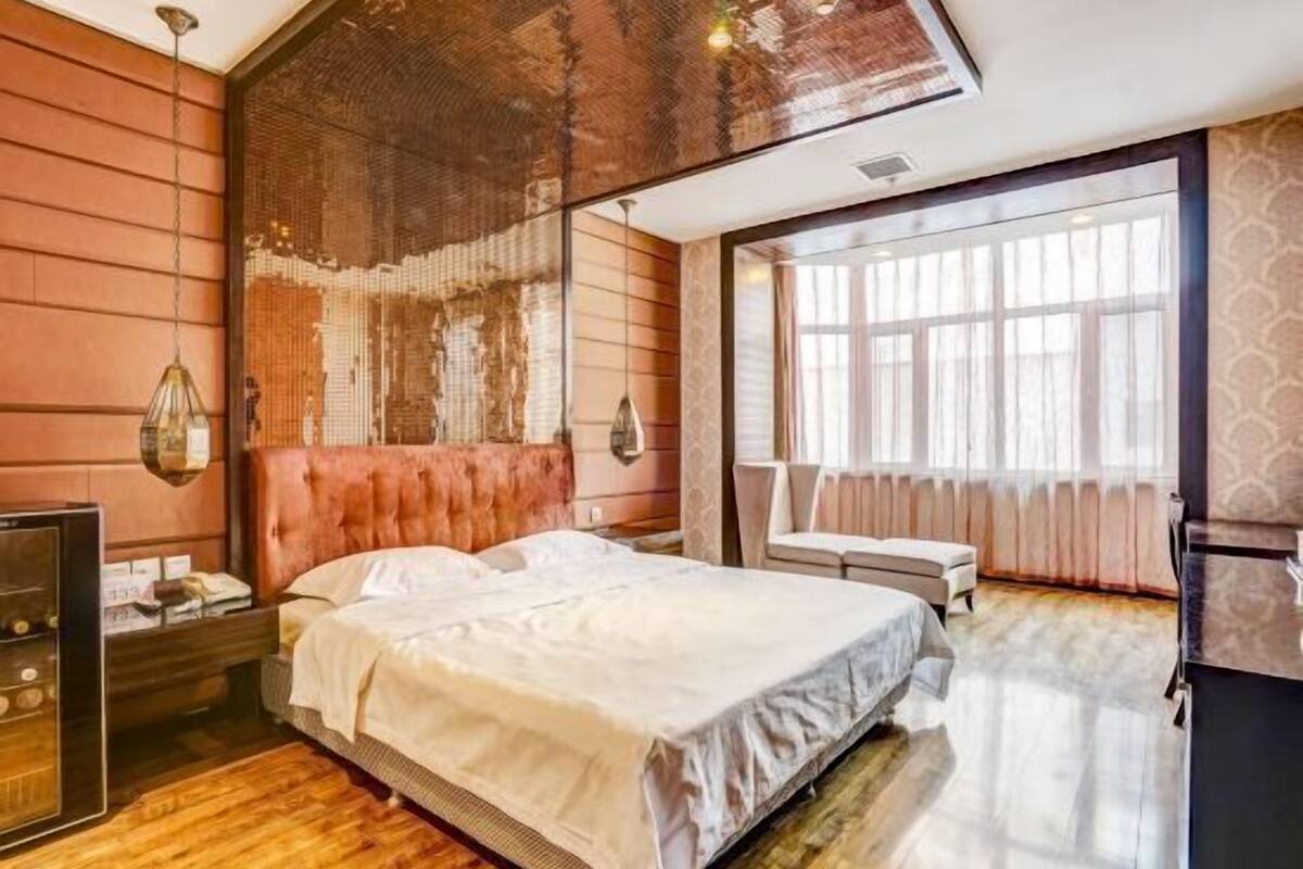 A bedroom with a large bed, a wooden floor, a mirror, and a window.