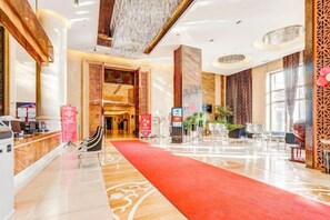 A hotel lobby with a red carpet, reception desk, and seating area. - Roman Garden Business Center (Mudanjiang)