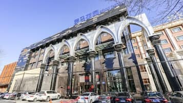 A building with a modern architectural style, featuring arched windows and columns. There are several cars parked in front, and a clear sky above.