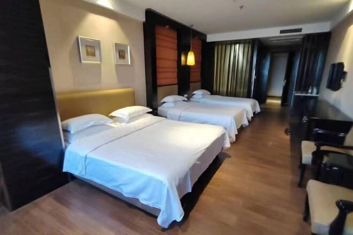 A hotel room with three beds, a wooden floor, a desk with a chair, and a television.