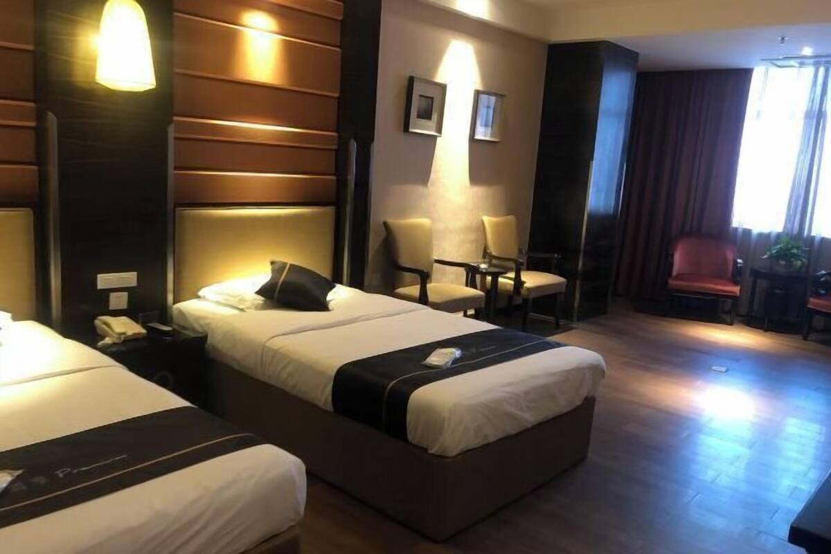 A hotel room with two beds, a sitting area with chairs, a desk, and a large window with curtains.