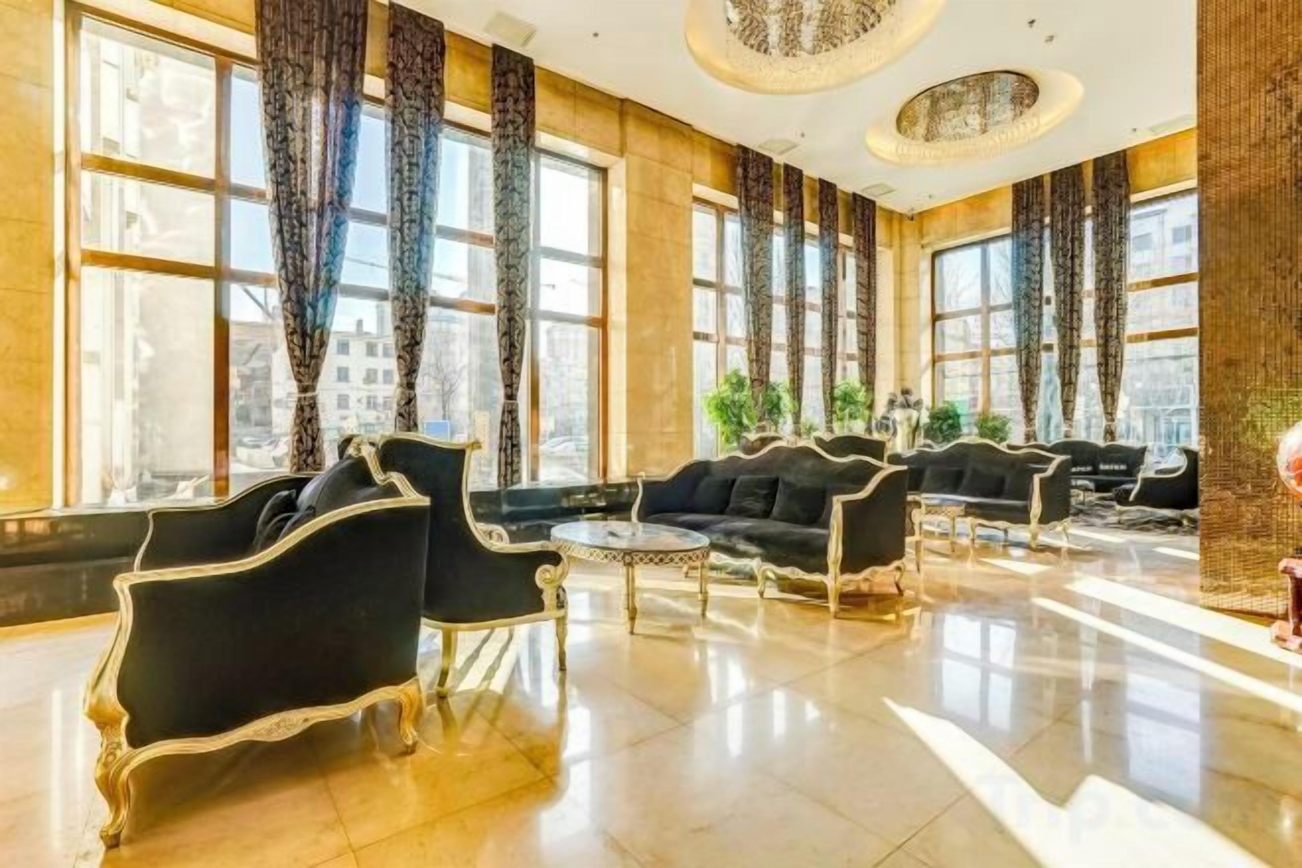 A spacious lobby with black leather sofas, a coffee table, and large windows with curtains.