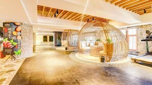 A spacious lobby with a high ceiling, wooden beams, and a stone wall. There are wicker seating areas and a large poster on the wall. - Roman Garden Business Center (Mudanjiang)