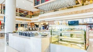 A multi-level shopping mall with a central food display area featuring a glass case with baked goods. - Roman Garden Business Center (Mudanjiang)