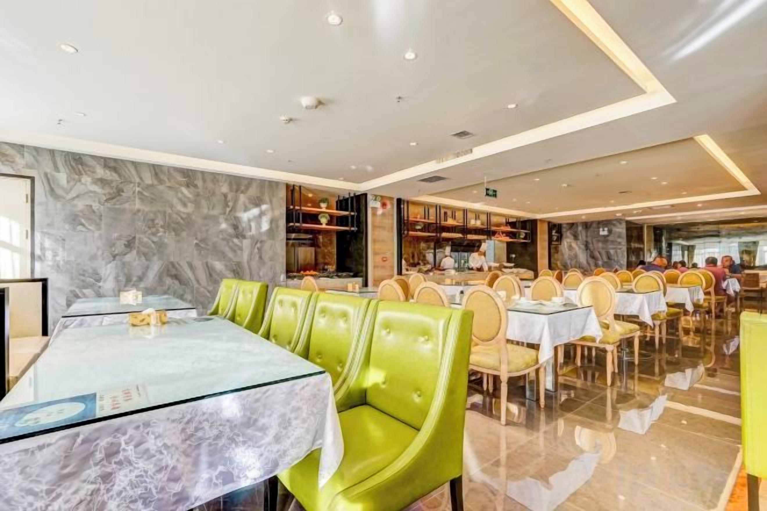 A restaurant with marble walls, green upholstered chairs, and tables with glass tops.