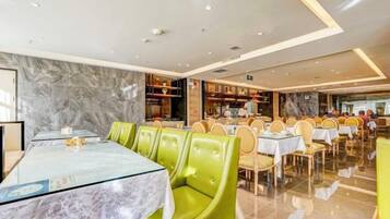 A restaurant with marble walls, green upholstered chairs, and tables with glass tops.