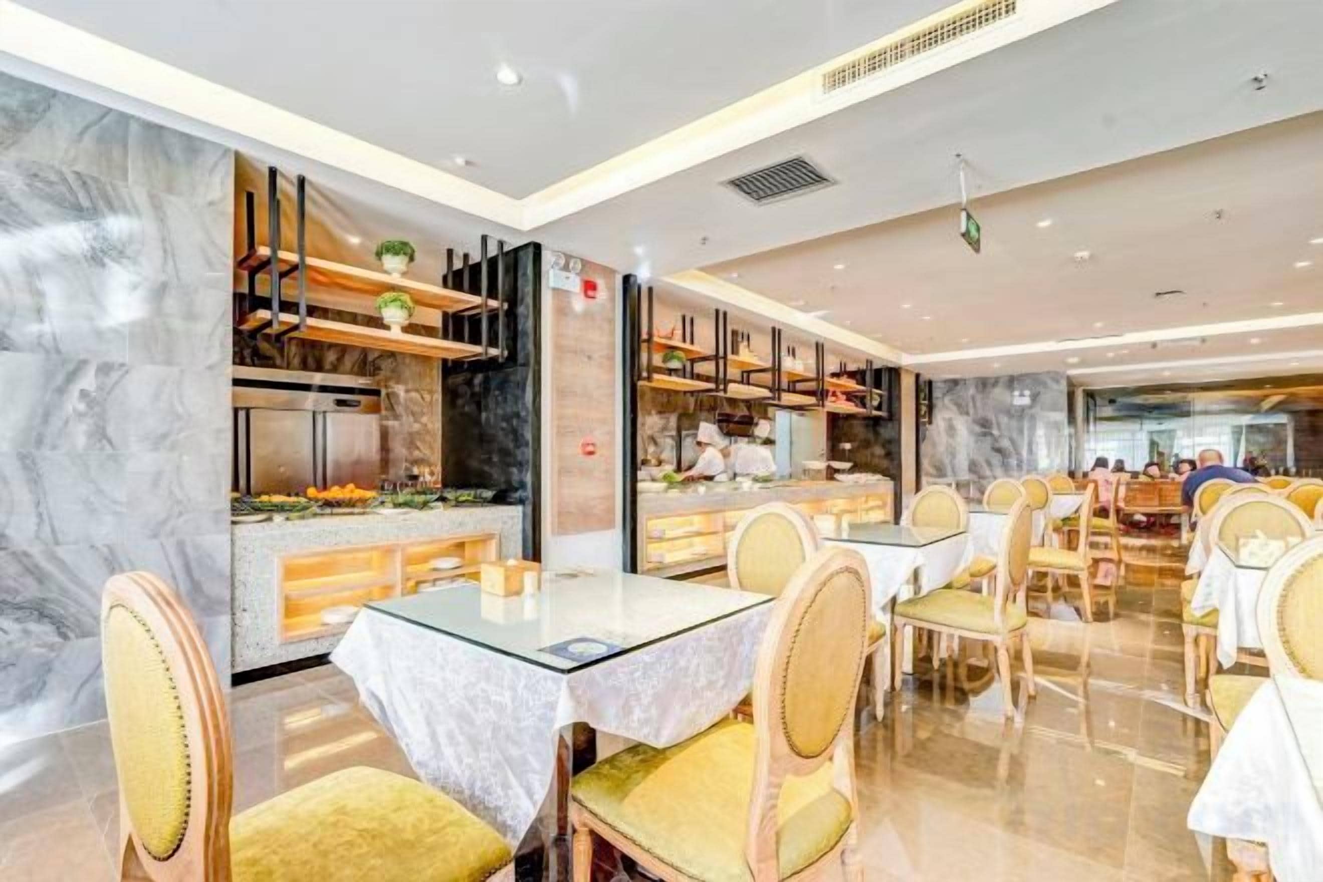 Un interno ristorante moderno con pareti in marmo, tavoli in vetro e sedie imbottite gialle.