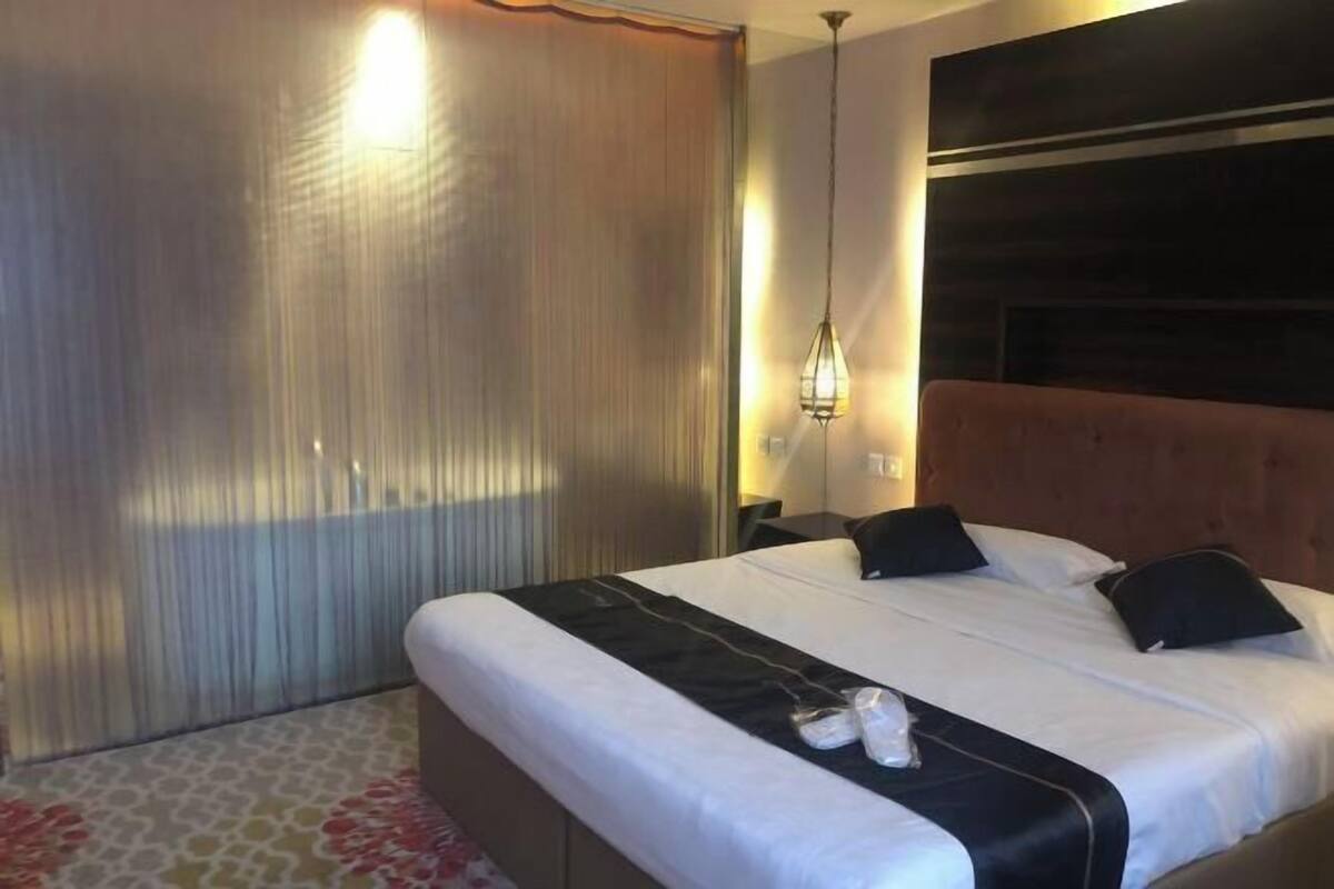 A hotel room with a large bed, a headboard, a bedside table, and a curtain.