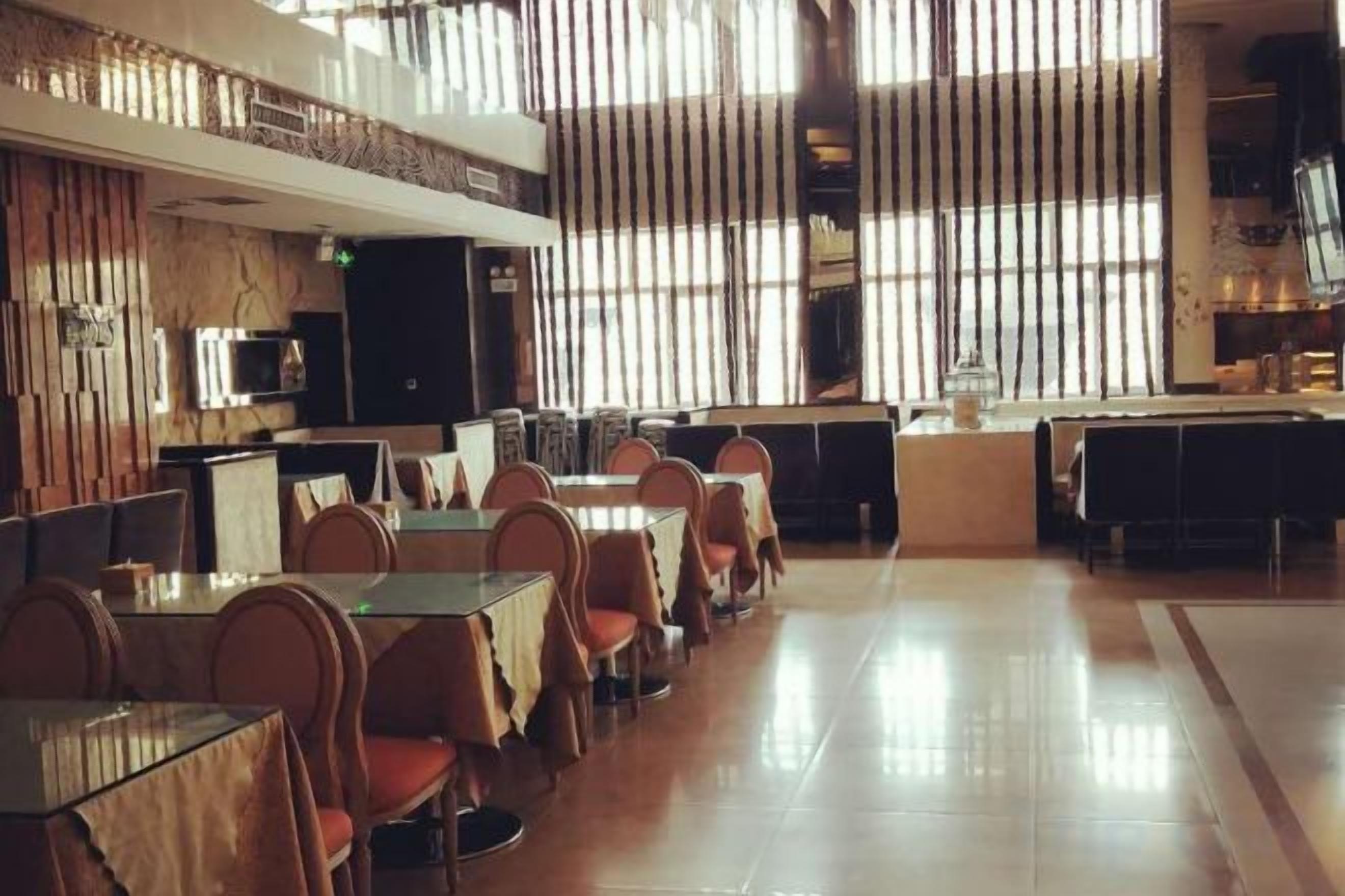 Un restaurante amplio con techos altos y ventanas grandes, que cuenta con varias mesas y sillas para comer.