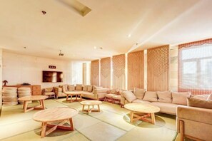 A spacious living area with multiple seating options, including sofas and round tables, and a television mounted on the wall. - Roman Garden Business Center (Mudanjiang)