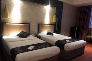 A hotel room with two beds, each with a headboard, a bedside table, and a lamp.