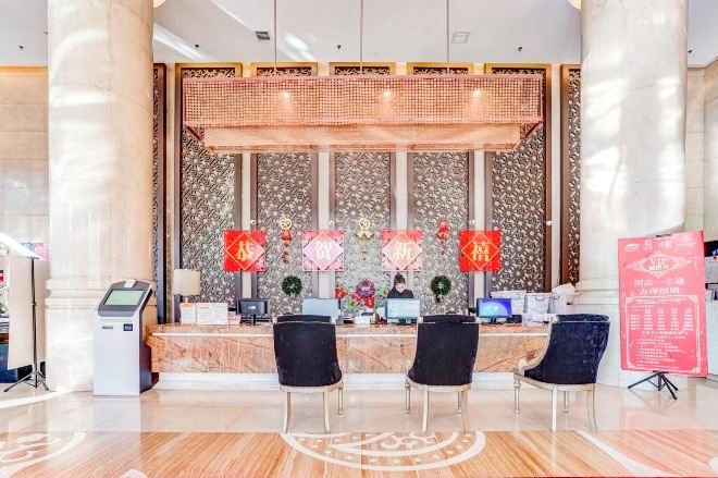 A reception area with a marble counter, two black chairs, a digital kiosk, and a decorative wall with red banners.