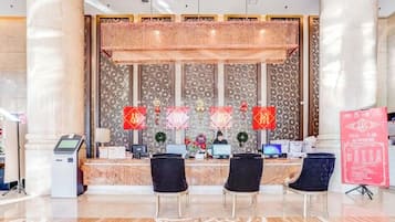 A reception area with a marble counter, two black chairs, a digital kiosk, and a decorative wall with red banners.