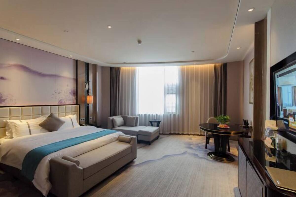 A modern hotel room with a large bed, a sofa, a small table, and a TV.