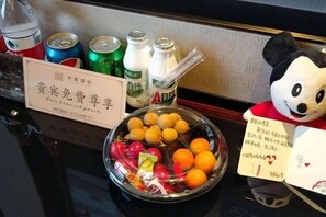 A table with a bowl of fruit, soda cans, and bottles, a plush toy, and a sign with Chinese characters.