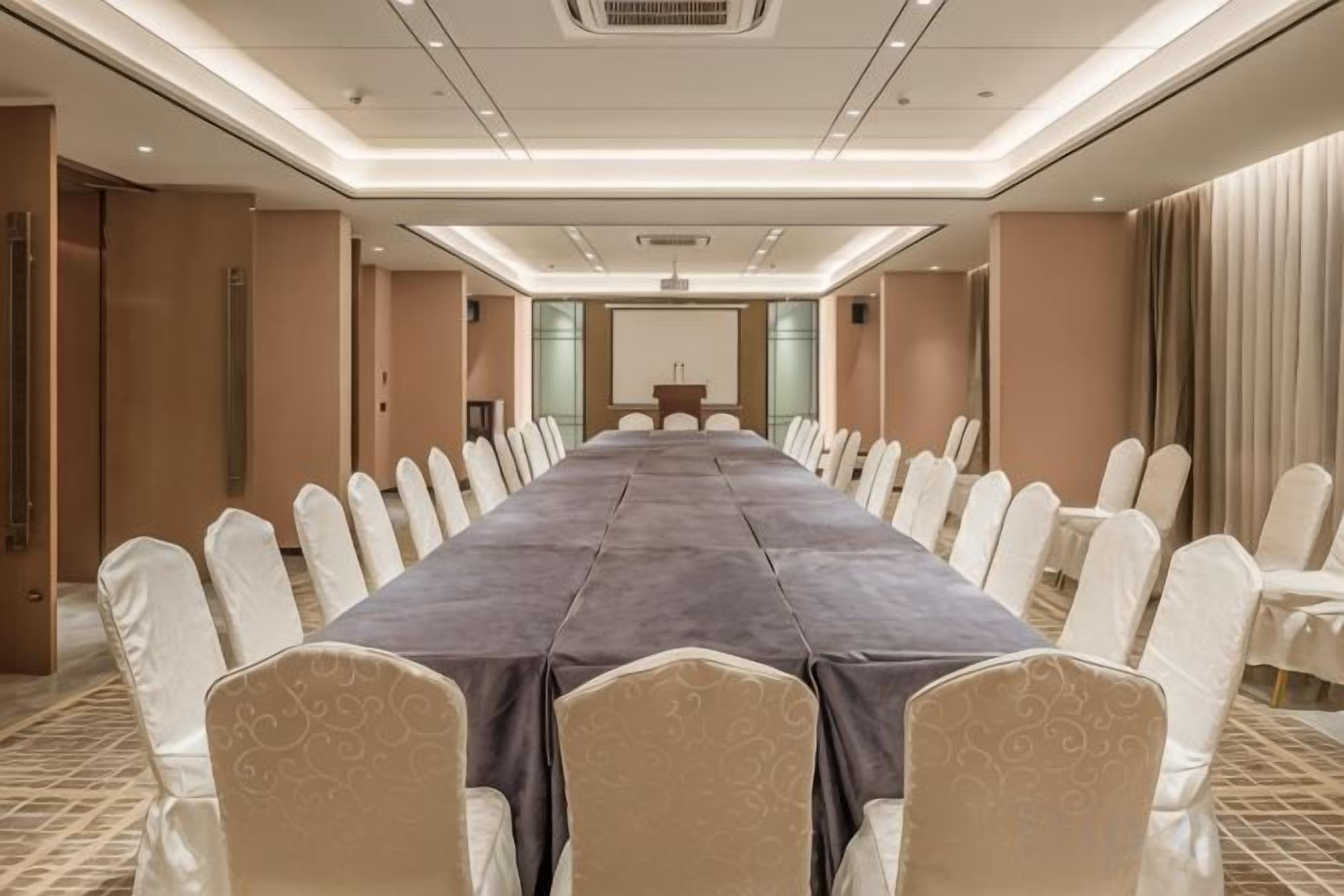 A conference room with a long table and chairs, a podium, and a carpeted floor.