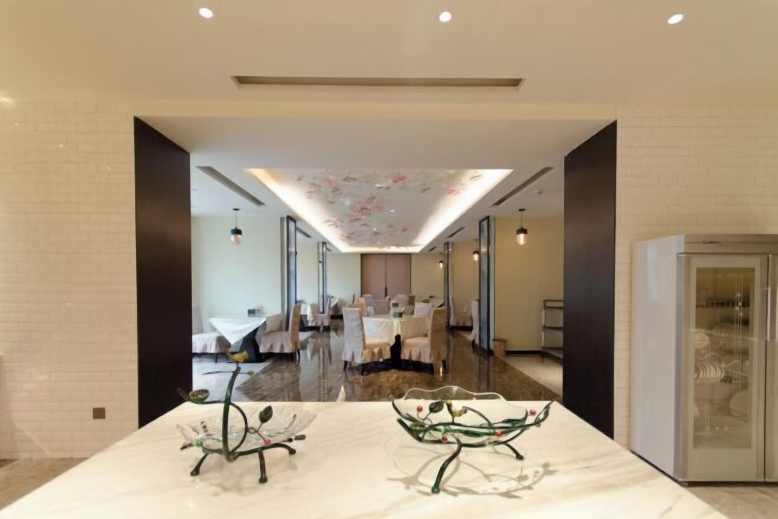 Un hall d’hôtel moderne avec un comptoir d’accueil en marbre, une vitrine et un espace repas en arrière-plan.