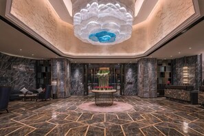 Un vestíbulo con piso de mármol, un arreglo floral central y una lámpara de techo decorativa de gran tamaño.