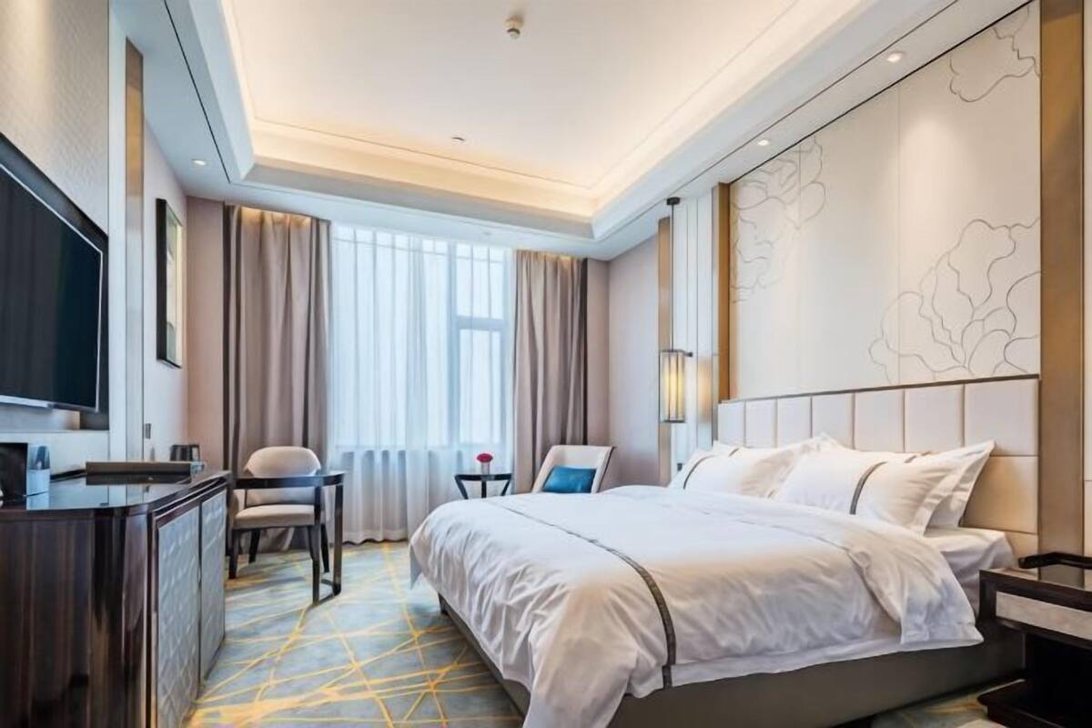 A hotel room with a bed, a desk, a chair, a TV, and a window with curtains.