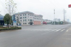 A building with a flat roof, large windows, and a crosswalk in front. - Huayi Hotel (Chongyang)