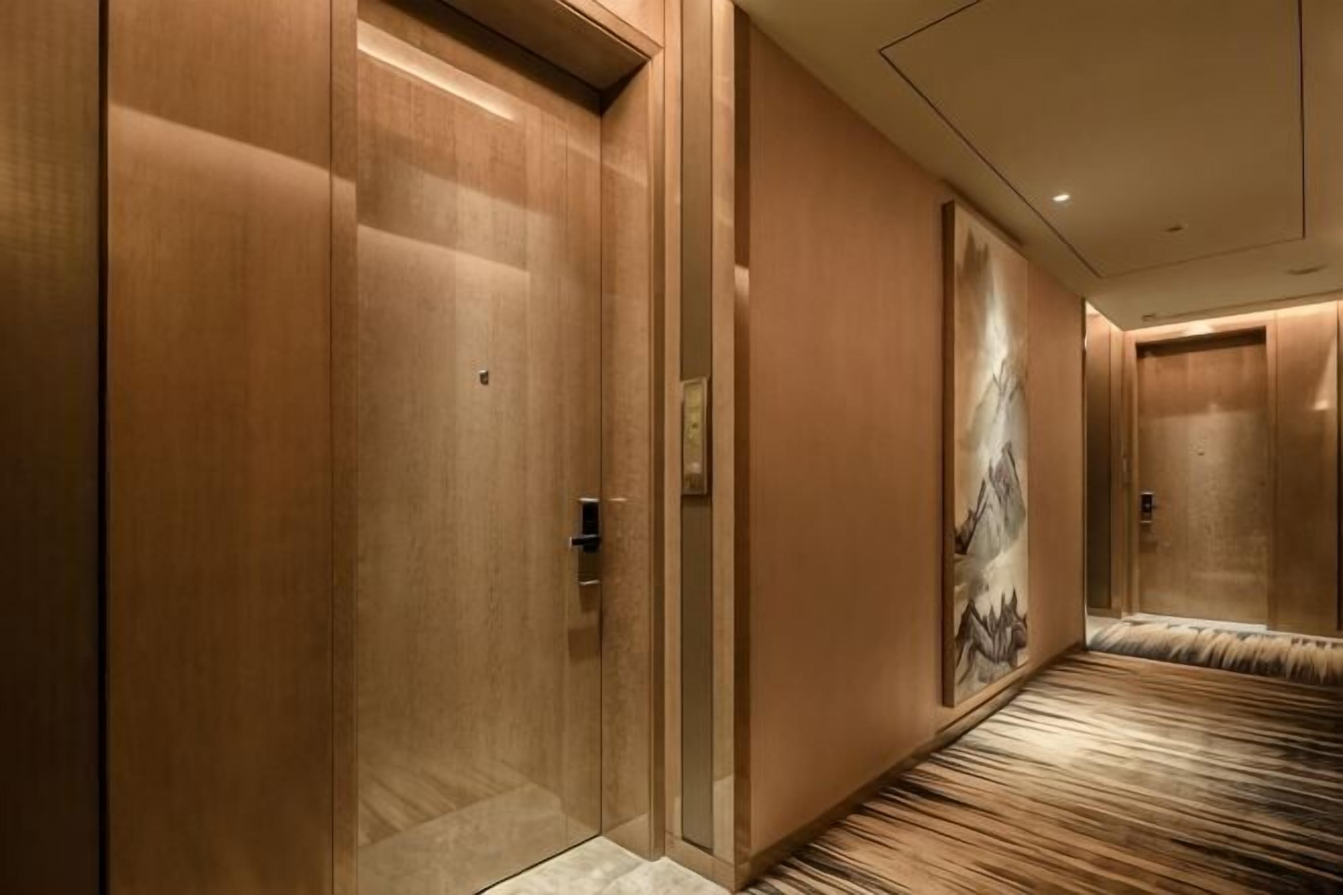 Un pasillo con puertas de madera, piso alfombrado y un cuadro de montañas en la pared.
