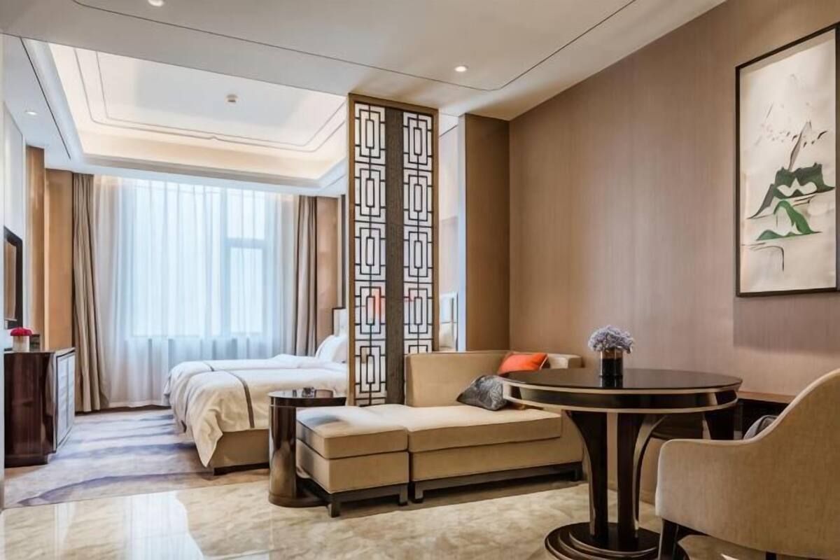 A hotel room with a bed, sofa, dining table, and a decorative screen.