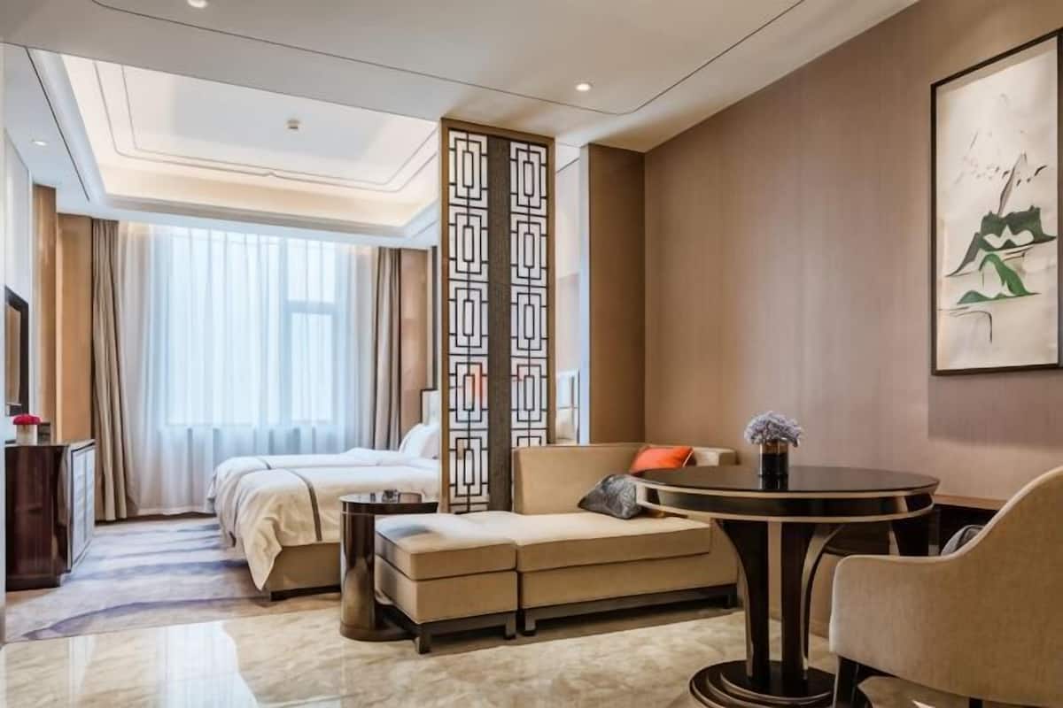 A hotel room with a bed, sofa, dining table, and a decorative screen.