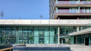 A modern building with large glass windows, a concrete facade, and a wooden bench in the foreground.