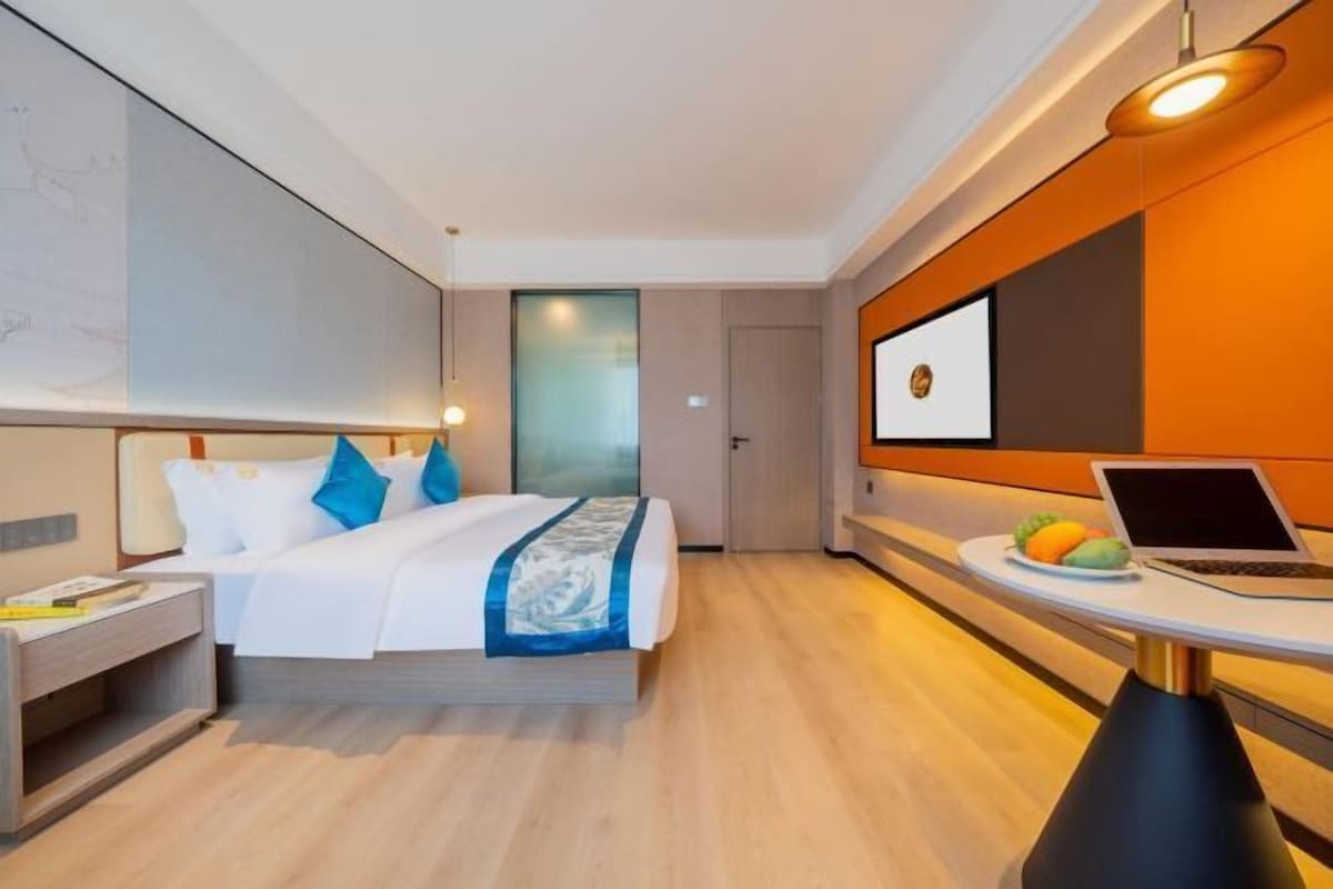 A modern hotel room with a bed, bedside table, and a laptop on a small table.