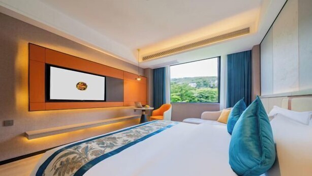 Habitación de hotel moderna con una cama grande, un televisor montado en la pared, una mesita y vistas al exterior con zonas verdes.