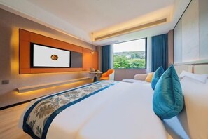 A modern hotel room with a large bed, a TV mounted on the wall, a small table, and a view of greenery outside. - Jinlong Hotel (Tianlin)