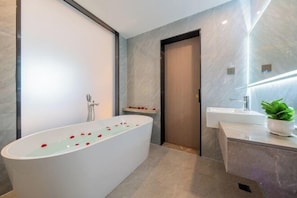 A modern bathroom with a freestanding bathtub, a vanity with a mirror, and a potted plant. - Jinlong Hotel (Tianlin)