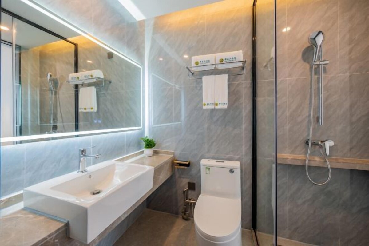 A modern bathroom with a large mirror, a white sink, a toilet, and a shower.