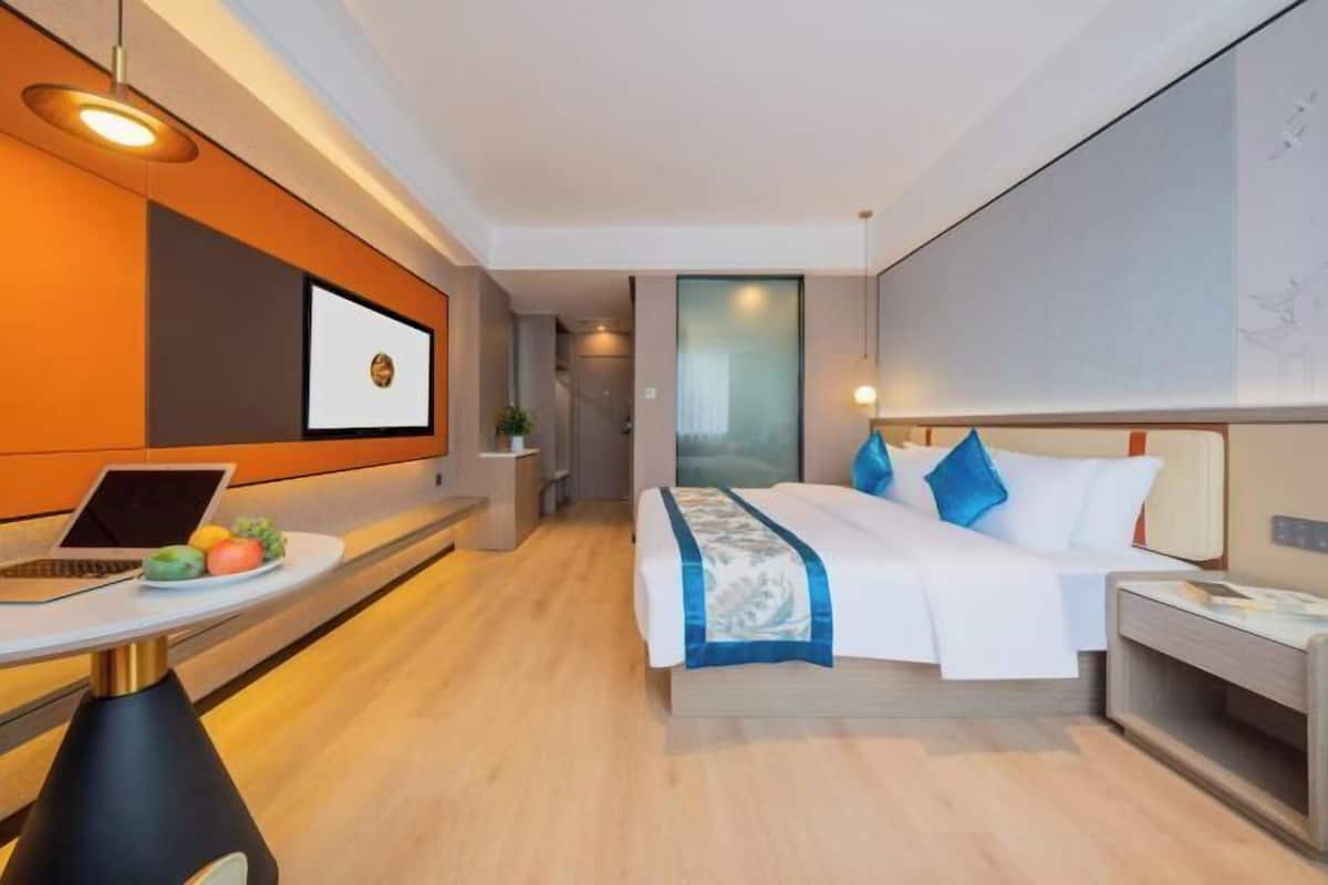 A modern hotel room with a bed, bedside table, and a desk with a laptop and fruit.