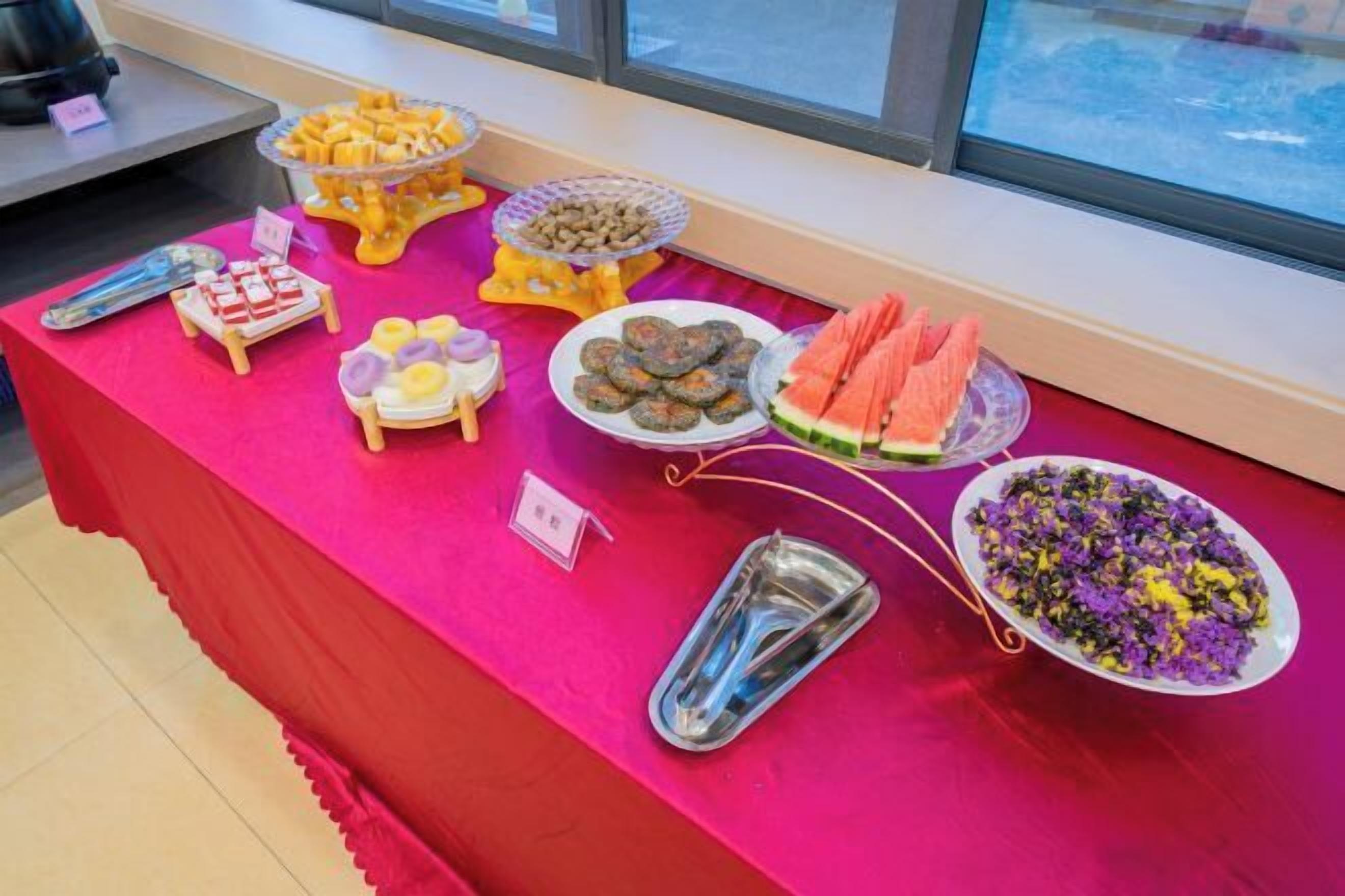 A buffet table with various food items including fruits, cookies, and a dish with purple flowers.