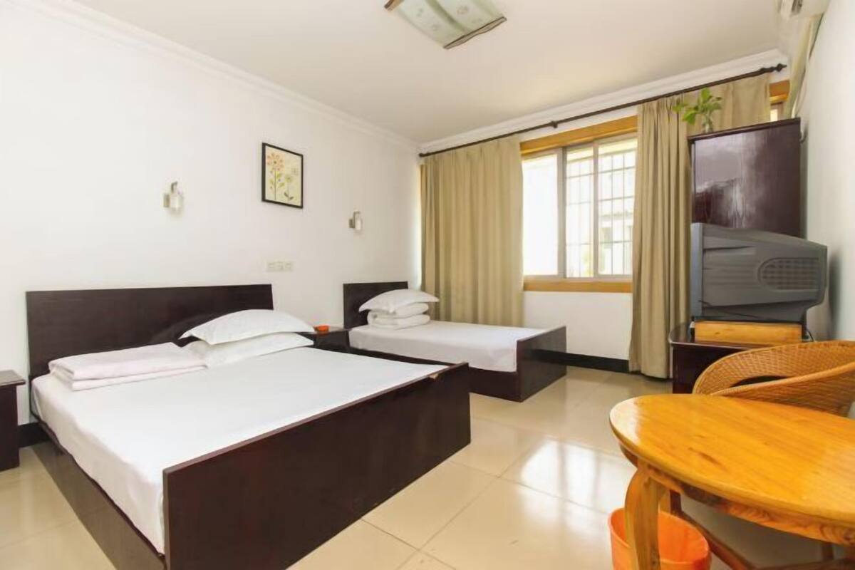A hotel room with two beds, a television, a wooden table, and a window with curtains.