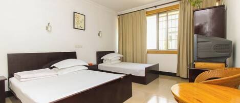 A hotel room with two beds, a television, a dining table, and a window with curtains.