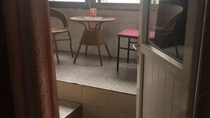 A small, enclosed outdoor seating area with a round table and two chairs, a small stool, and a window with a view of the outside. - Wan Fu Hostel (Kunshan)