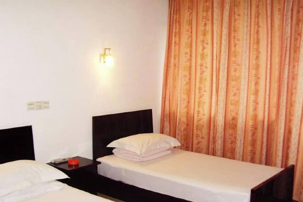 A single bed with a white mattress and pillows, a nightstand with a red object, and a wall-mounted light fixture.