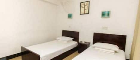 A room with two single beds, a nightstand, a wall-mounted light, and a framed picture.
