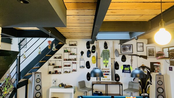 A room with a pool table, a staircase, and various motorcycle helmets and accessories on the walls.