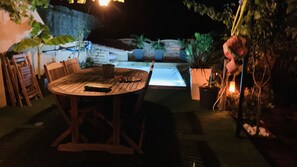 An outdoor patio area with a round wooden table and chairs, surrounded by potted plants and a small water feature.