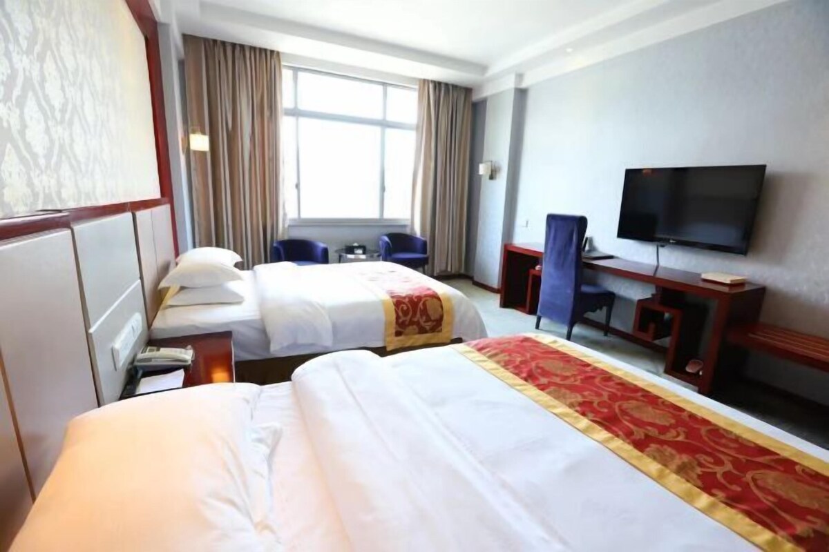 Une chambre d’hôtel avec deux lits, un bureau avec une chaise, une télévision et une fenêtre avec des rideaux.