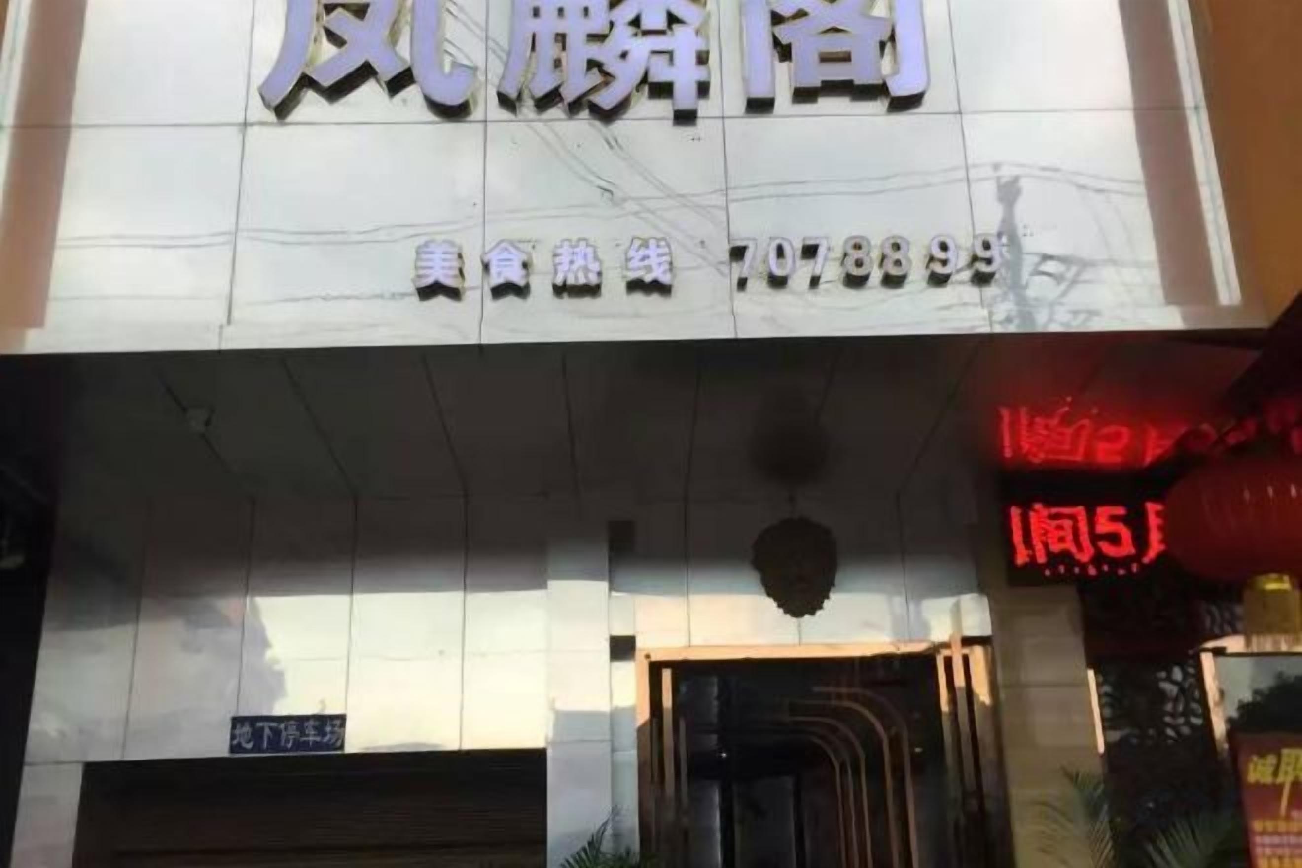 Entrada de hotel con un cartel sobre la puerta y una pantalla digital a la derecha.