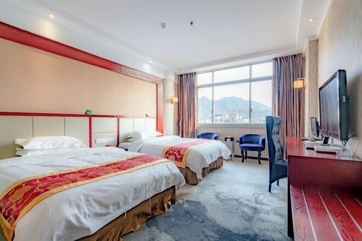 Une chambre d’hôtel avec deux lits, un bureau avec une télévision et une vue sur les montagnes par la fenêtre.