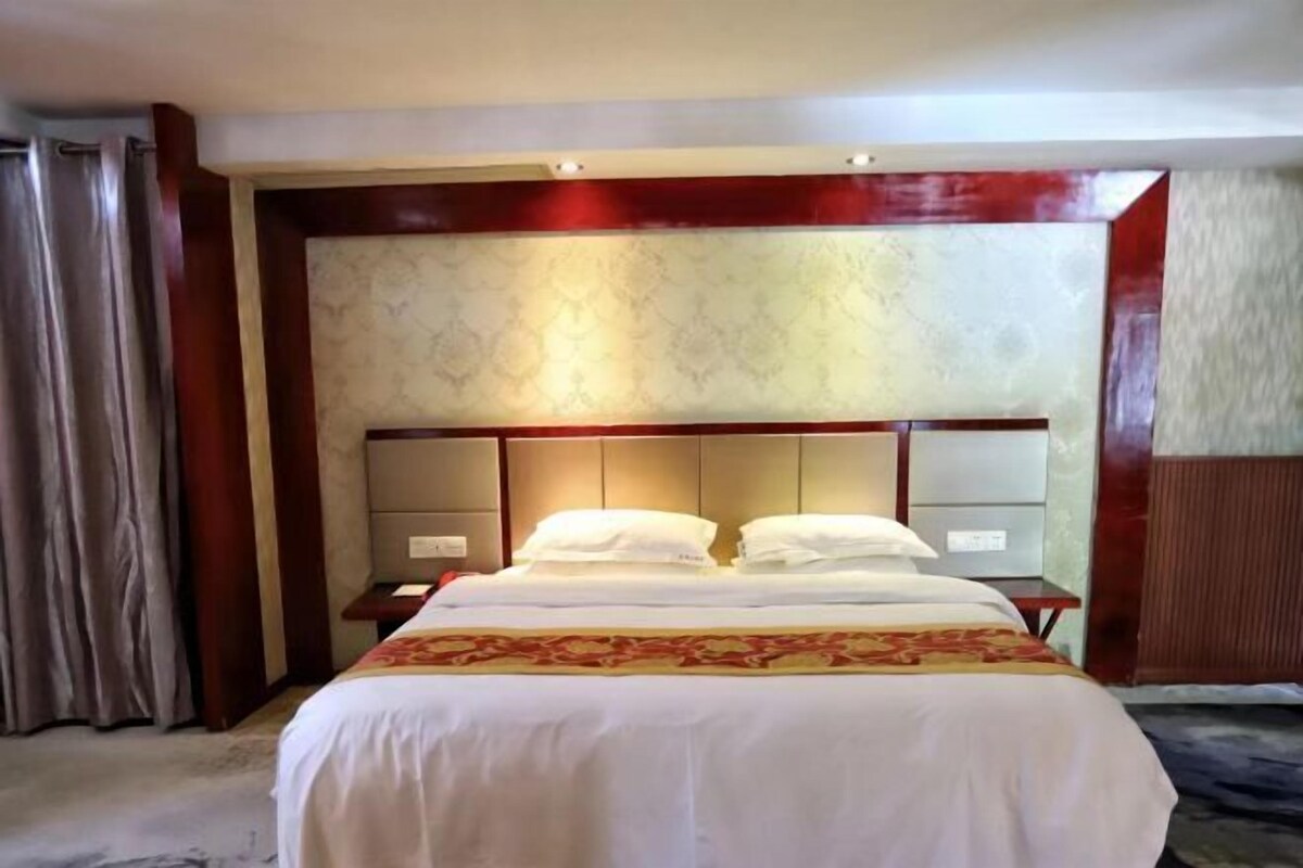 Une chambre d’hôtel avec un grand lit, une tête de lit dotée d’un éclairage intégré, une table de chevet et un rideau.
