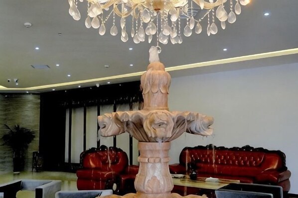 Un hall d’entrée agrémenté d’une grande fontaine en pierre, de canapés en cuir rouge et d’un lustre moderne.