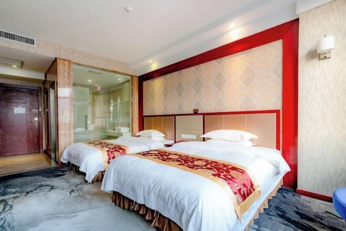 Une chambre d’hôtel avec deux lits, une cloison en verre et un mur d’accent rouge.
