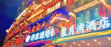 A hotel with multiple balconies, illuminated signage, and a traditional architectural style.